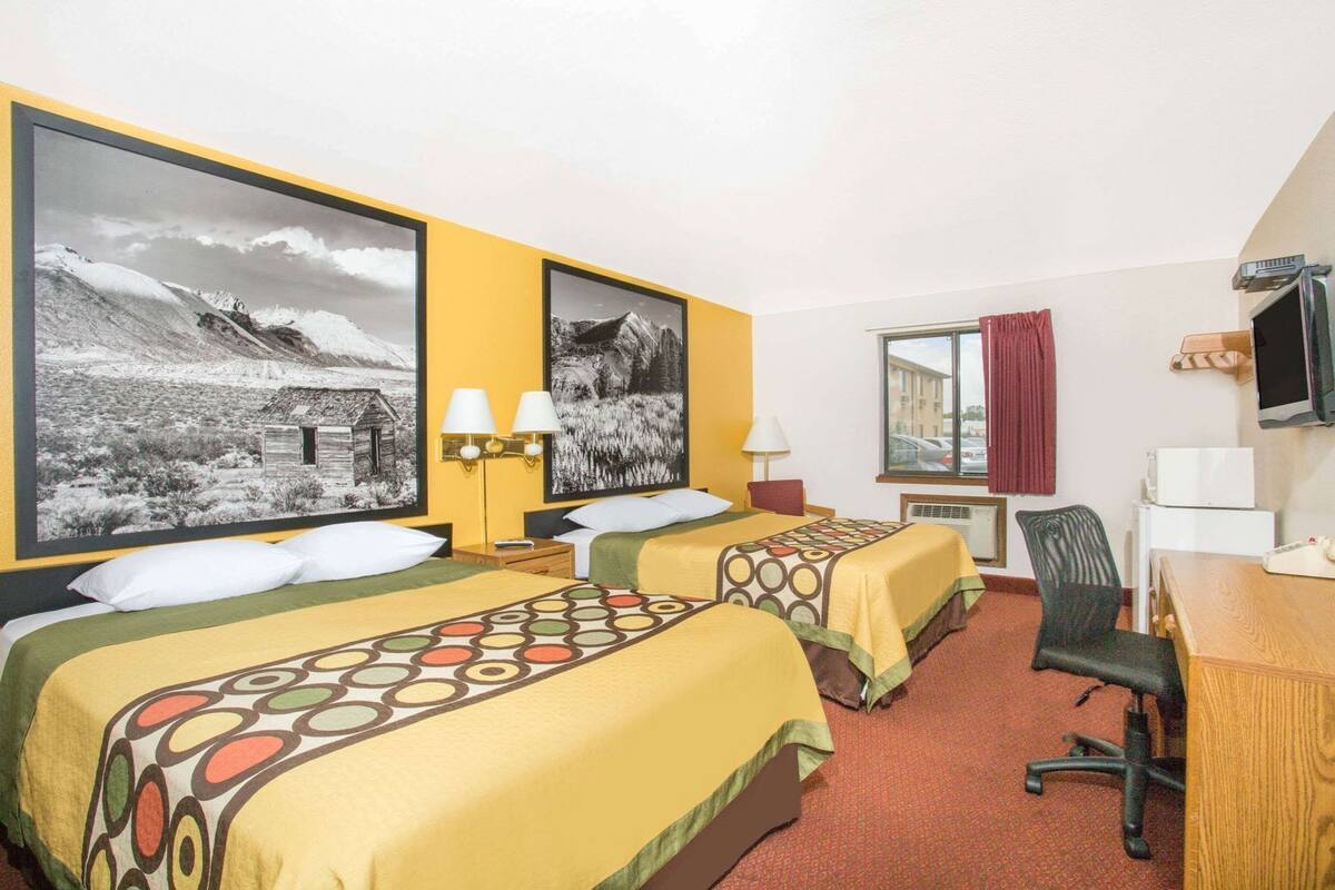 A hotel room with two beds, a desk, a chair, and a television.