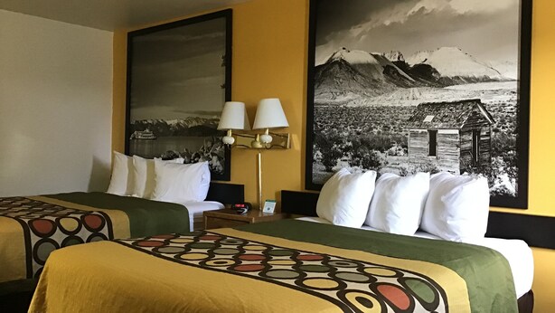 A hotel room with two beds, each with a patterned bedspread, a nightstand with a lamp, and a large black and white landscape painting on the wall. - Super 8 by Wyndham Elko (Elko)