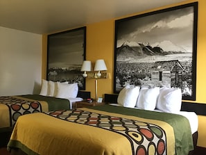 A hotel room with two beds, each with a patterned bedspread, a nightstand with a lamp, and a large black and white landscape painting on the wall. - Super 8 by Wyndham Elko (Elko)