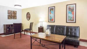 A room with a wooden coffee table, a black leather sofa, a dining table with chairs, a cabinet, and two wall-mounted clocks. - Super 8 by Wyndham Elko (Elko)