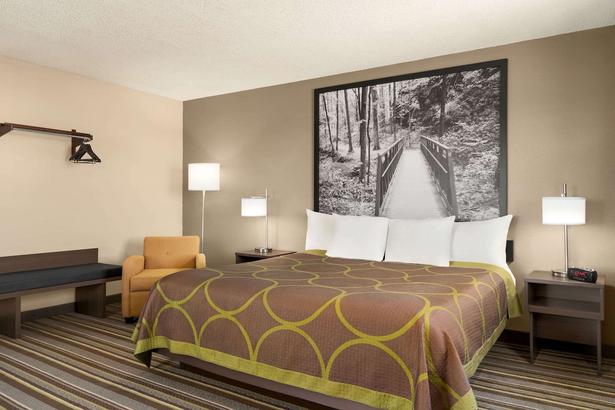 A hotel room with a large bed, a bench, a chair, two bedside tables with lamps, and a large framed picture on the wall.