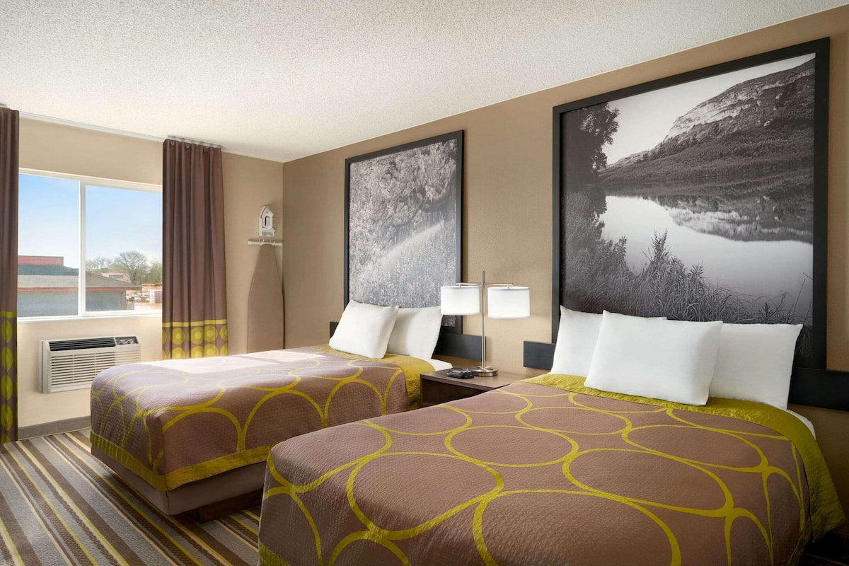 A hotel room with two beds, a large window with curtains, a flat-screen TV, and a large framed picture on the wall.