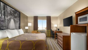 A hotel room with a large bed, a desk, a chair, a television, and a refrigerator. - Super 8 by Wyndham Liberal KS (Liberal)