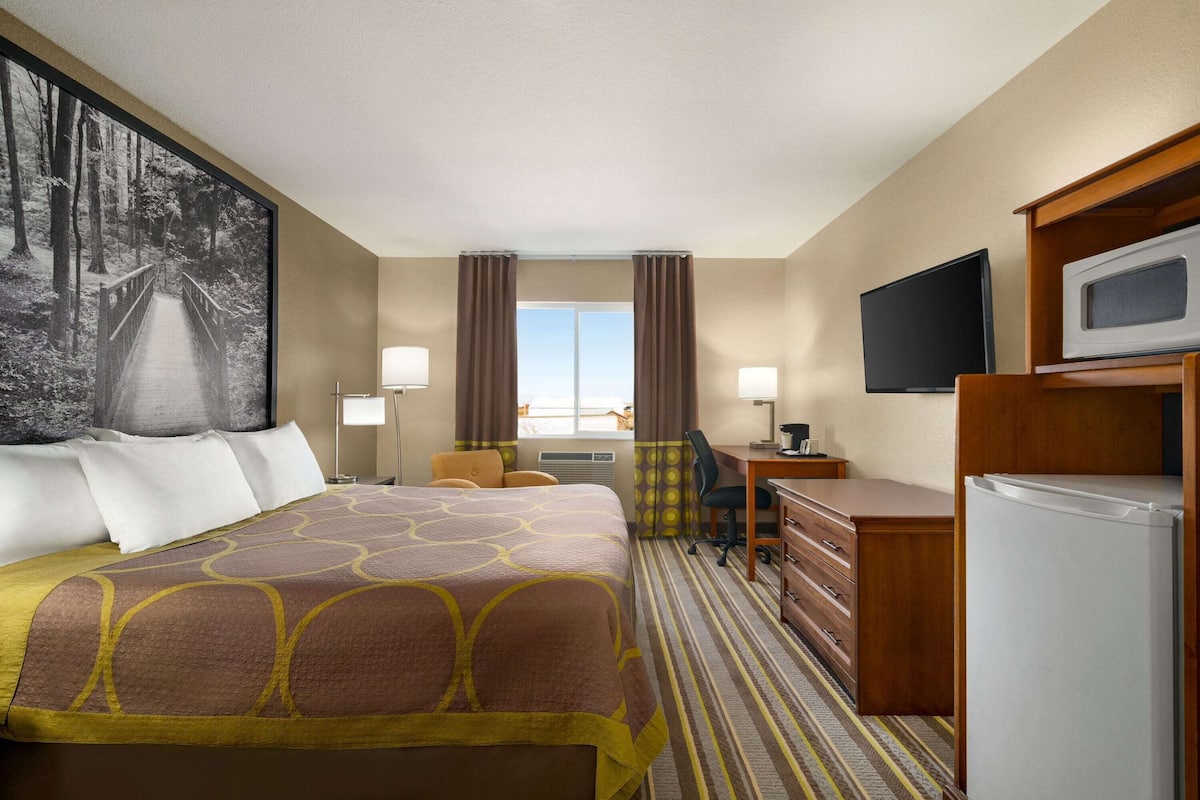 A hotel room with a large bed, a desk, a chair, a television, and a refrigerator.