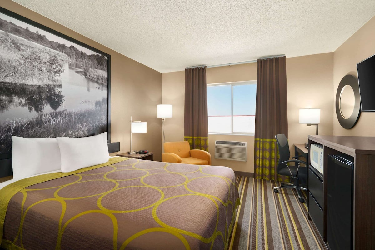 A hotel room with a large bed, a desk with a computer, a chair, a TV, and a window with curtains.