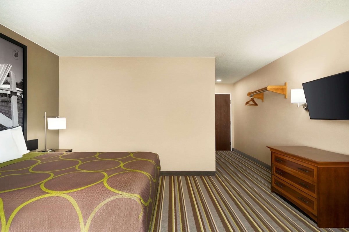 A hotel room with a bed, a dresser, a television, and a lamp.