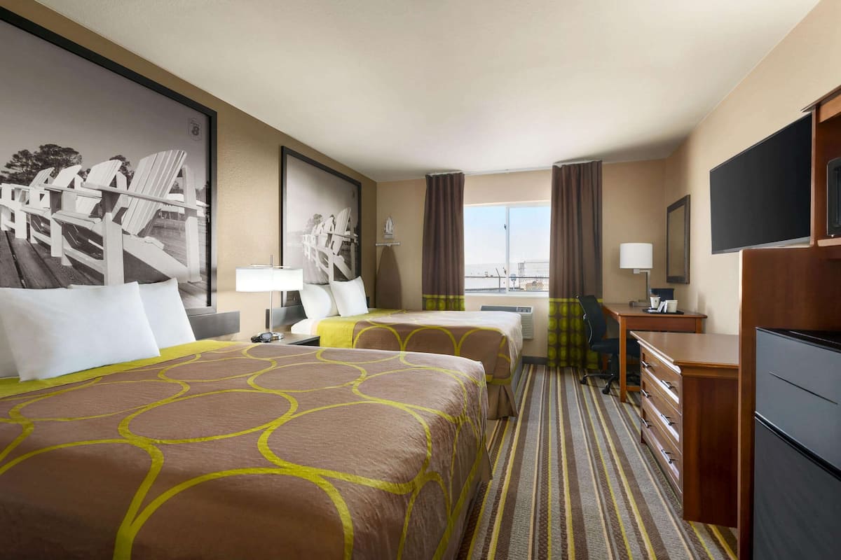 A hotel room with two beds, a desk, a chair, a TV, and a window with curtains.