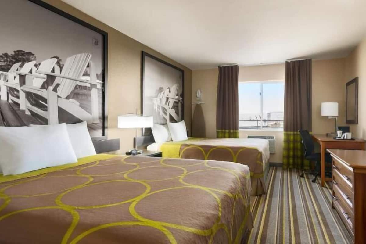 A hotel room with two beds, a desk, a chair, a television, and a large window with curtains.