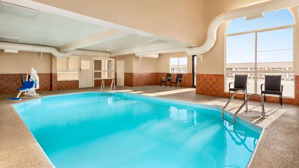 An indoor swimming pool with clear blue water, a diving board, and a seating area with chairs. - Super 8 by Wyndham Liberal KS (Liberal)
