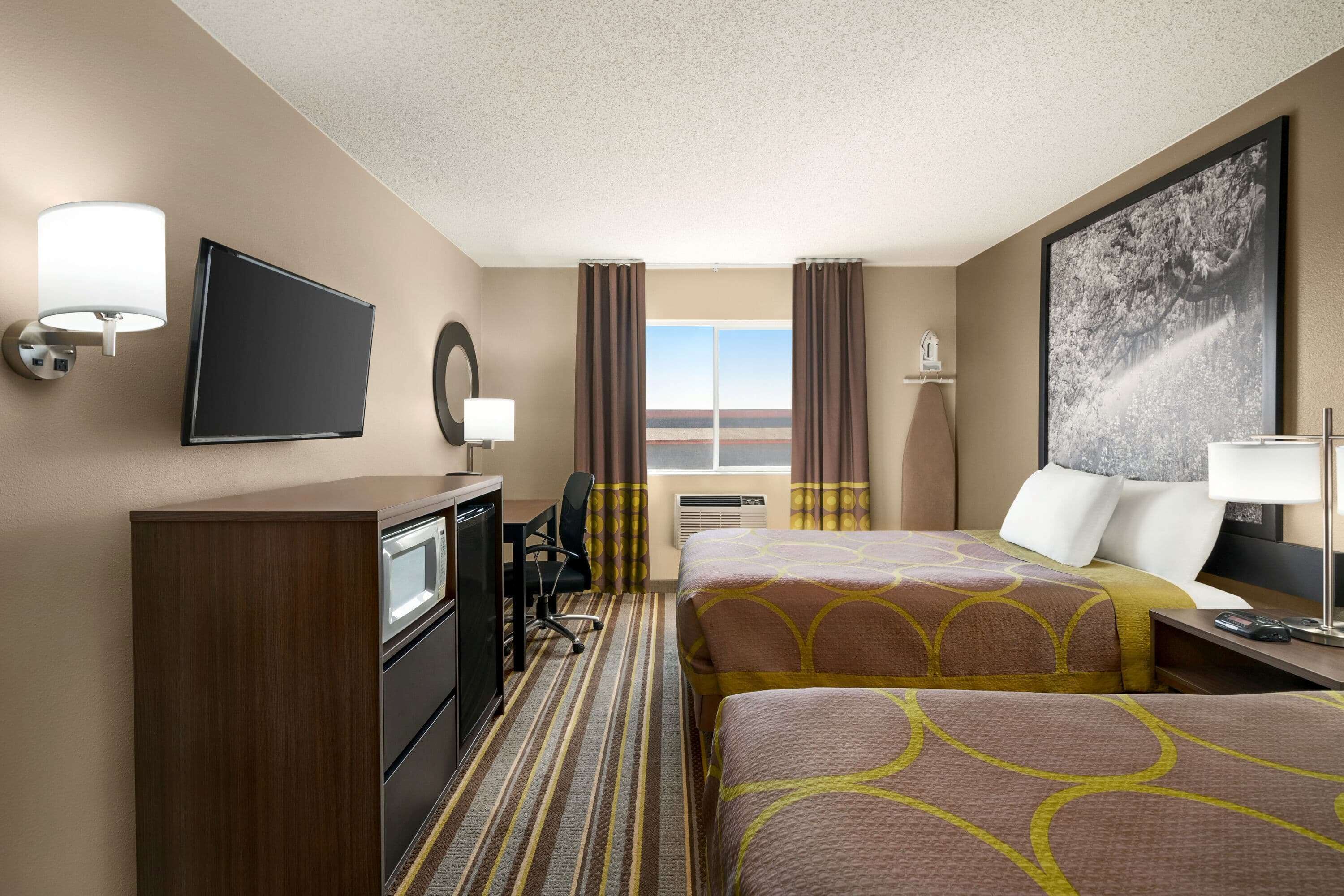 Une chambre d’hôtel avec deux lits, un bureau, une télévision et une fenêtre avec des rideaux.