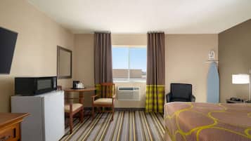 Une chambre d’hôtel comprenant un lit, un bureau avec un micro-ondes, une chaise, une petite table, un appareil de climatisation et une fenêtre avec des rideaux.