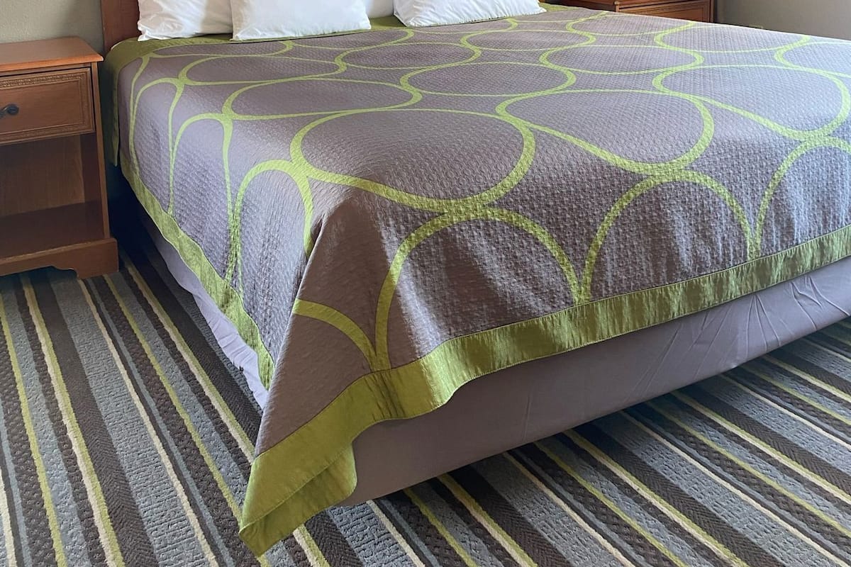 A hotel room with a bed, wooden headboard, two bedside tables, a nightstand, a wall-mounted ironing board, and a mirror.