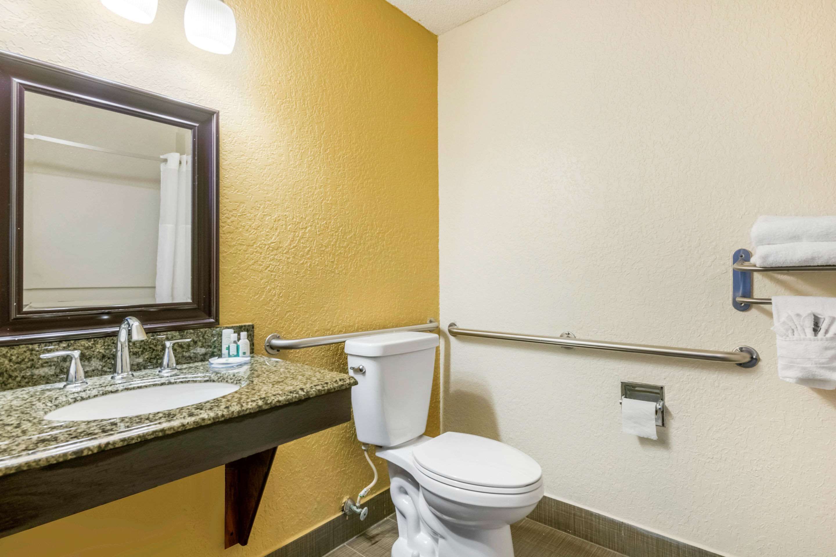 A bathroom with a granite sink, a white toilet, a mirror, and a towel rack.
