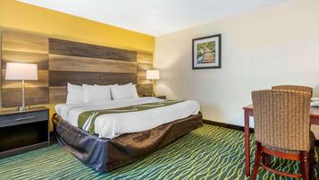 Habitación de hotel con cama, dos mesitas de noche con lámparas, una silla de mimbre y una alfombra estampada.