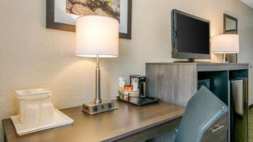 Habitación de hotel con un escritorio de madera, dos lámparas, un televisor, una cafetera y un refrigerador.