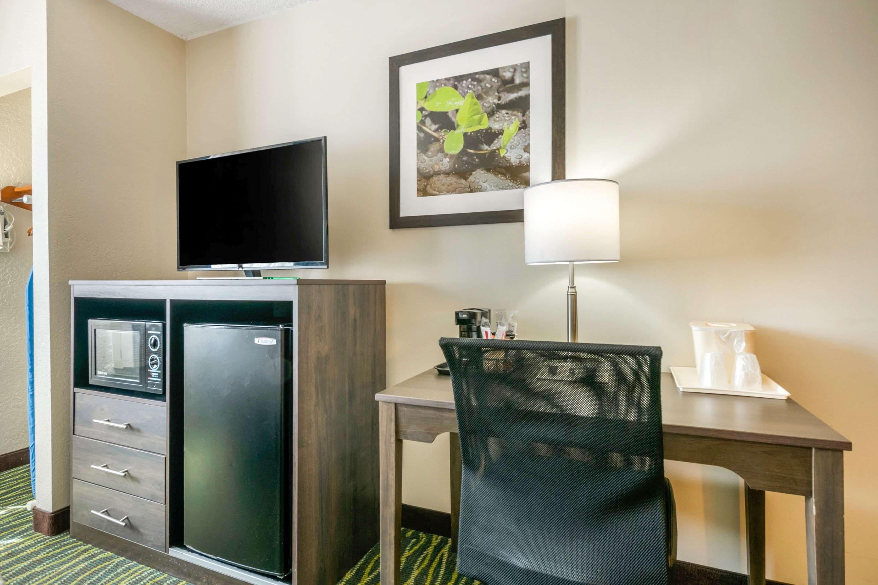 Une chambre d’hôtel équipée d’un téléviseur à écran plat, d’un réfrigérateur, d’un bureau avec une chaise, d’une lampe et d’un tableau encadré au mur.