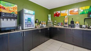 A kitchen area with a juice dispenser, refrigerator, coffee maker, and waffle maker. - Quality Inn & Suites Leesburg Chain of Lakes (Leesburg)