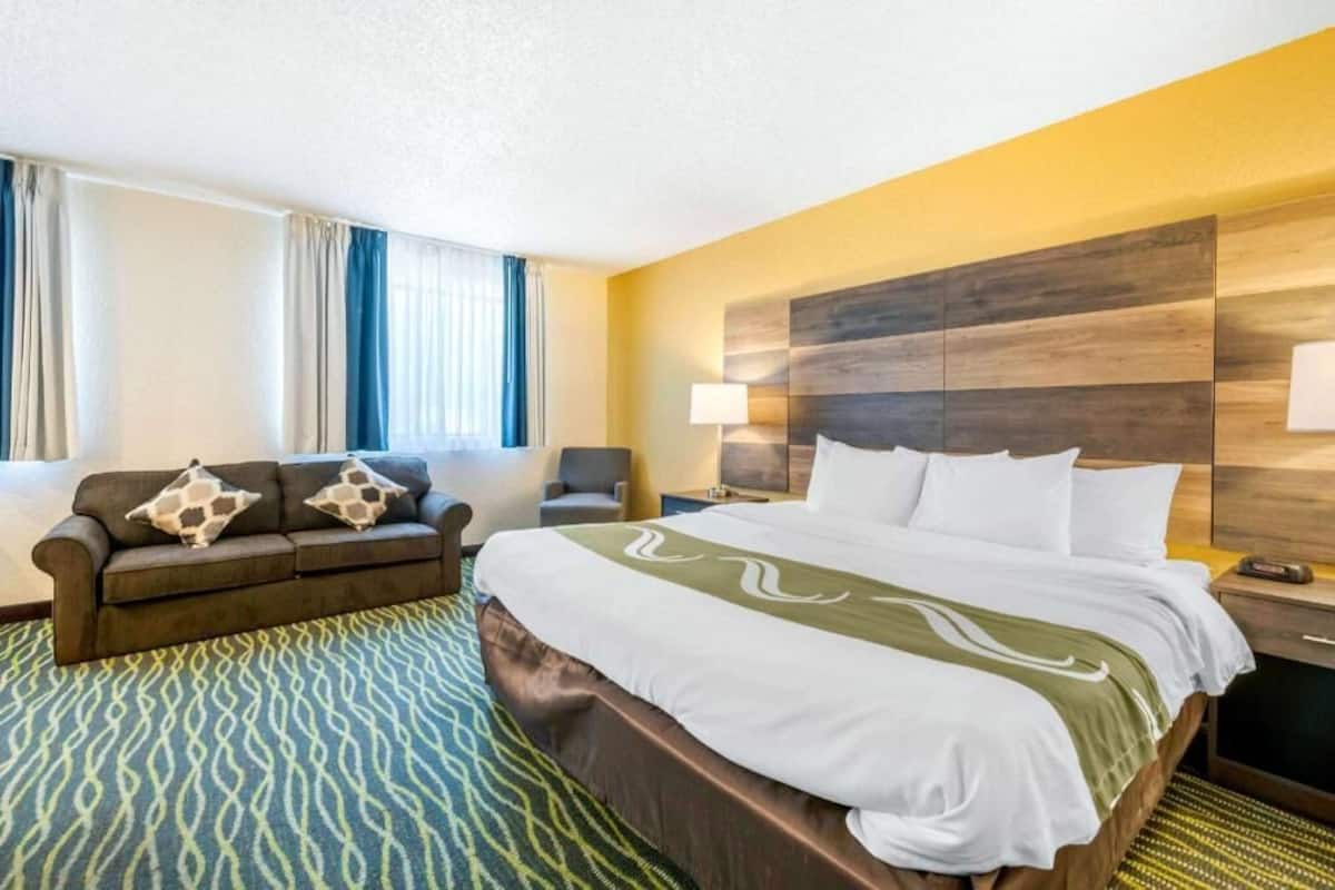 A hotel room with a bed, a sofa, a nightstand, a lamp, and a window with curtains.