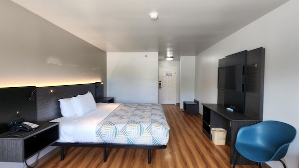 A hotel room with a bed, bedside table, desk, chair, TV, and a door.