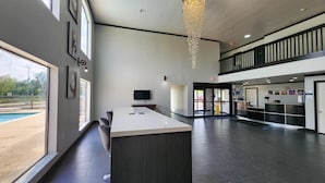 A spacious, modern hotel lobby with a large reception desk, a pool view, and a high ceiling with a decorative light fixture. - Motel 6 Ennis, TX (Ennis)