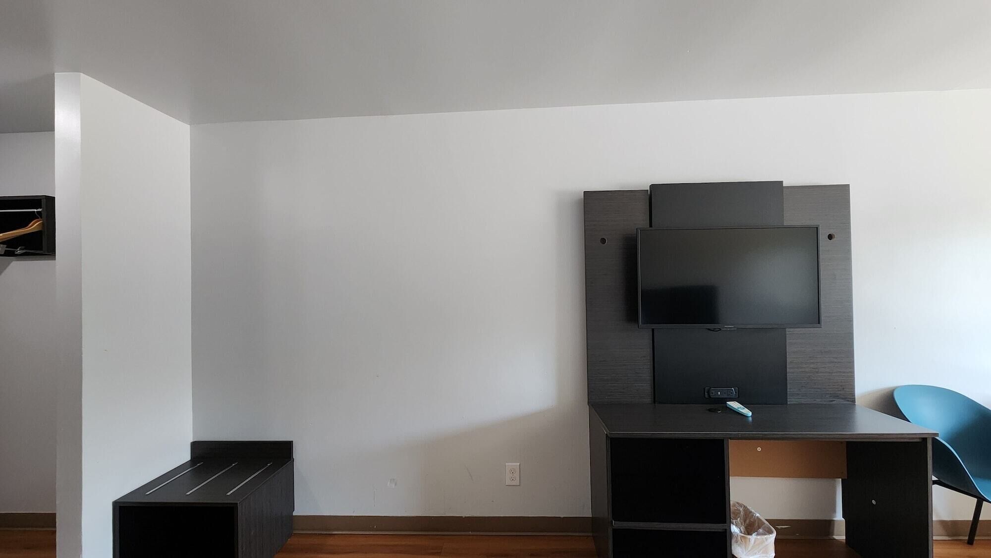 Una habitación moderna con una televisión de pantalla plana montada en la pared, un escritorio con una silla y un pequeño cubo de basura.