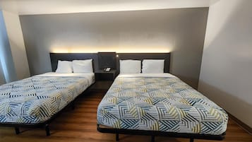 A hotel room with two single beds, each with a patterned bedspread and white pillows. There is a nightstand with a lamp between the beds.