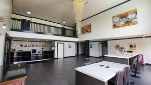 A spacious lobby with a reception desk, a seating area with tables and chairs, and a staircase leading to an upper level. - Motel 6 Ennis, TX (Ennis)