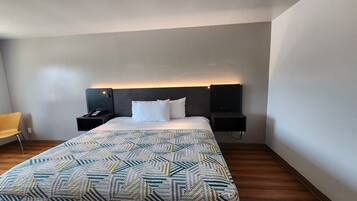 Une chambre d’hôtel avec un lit, une table de chevet, une chaise et un téléviseur fixé au mur.