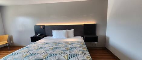 Une chambre d’hôtel avec un lit, une table de chevet, une chaise et un téléviseur fixé au mur.