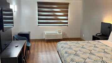 Un dormitorio con cama, escritorio, silla, ventana con persianas, ventilador de techo y unidad de aire acondicionado.