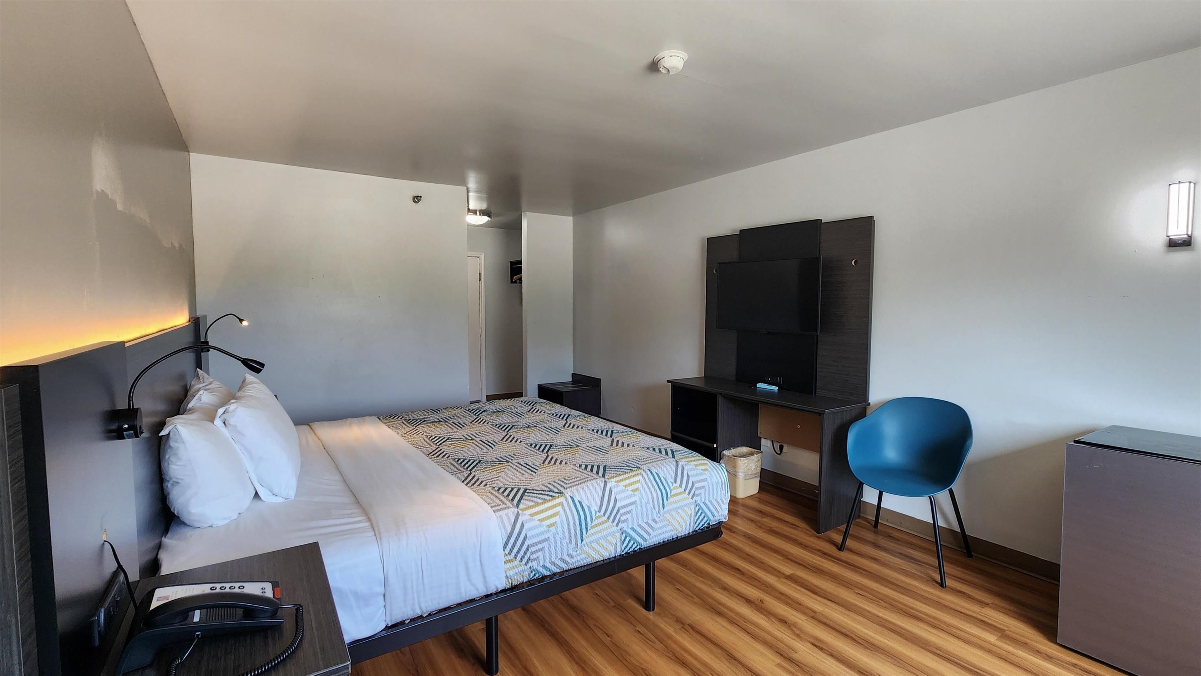 Ett modernt hotellrum med en säng, ett skrivbord, en stol och en TV.