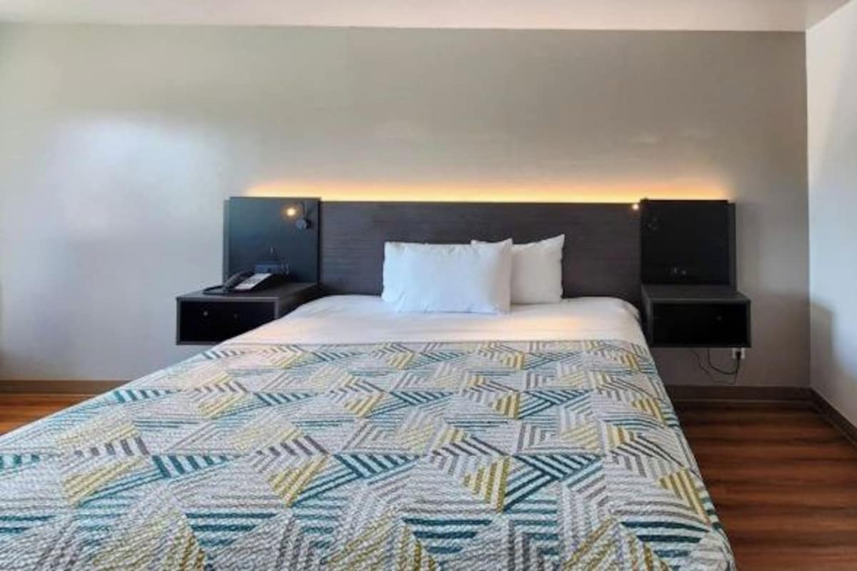 Una habitación de hotel con cama, dos mesitas de noche y cabecero con iluminación integrada.