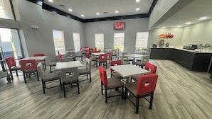 A modern dining area with multiple tables and chairs, large windows, and a kitchen counter.