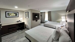 A hotel room with two beds, a desk, a TV, and a window with curtains. - Quality Inn & Suites at Airport Blvd I-65 (Mobile)