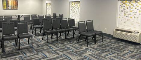 Un salón de conferencias con filas de sillas, piso alfombrado y un equipo de aire acondicionado grande.
