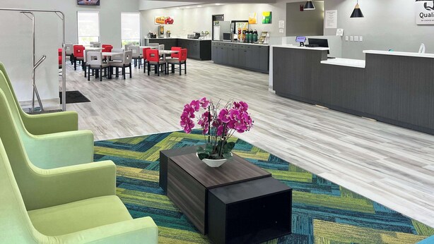 A modern hotel lobby with a reception desk, seating area, and a kitchen in the background. - Quality Inn & Suites at Airport Blvd I-65 (Mobile)