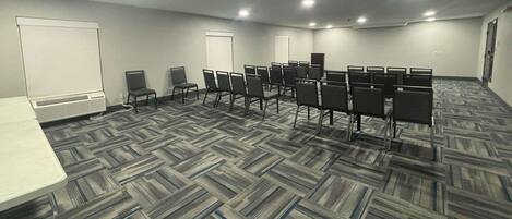 A conference room with a carpeted floor, rows of chairs, a whiteboard, and a door.