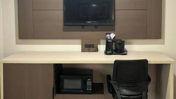 Un espacio de trabajo compacto con televisor de pantalla plana, cafetera, microondas y una silla.