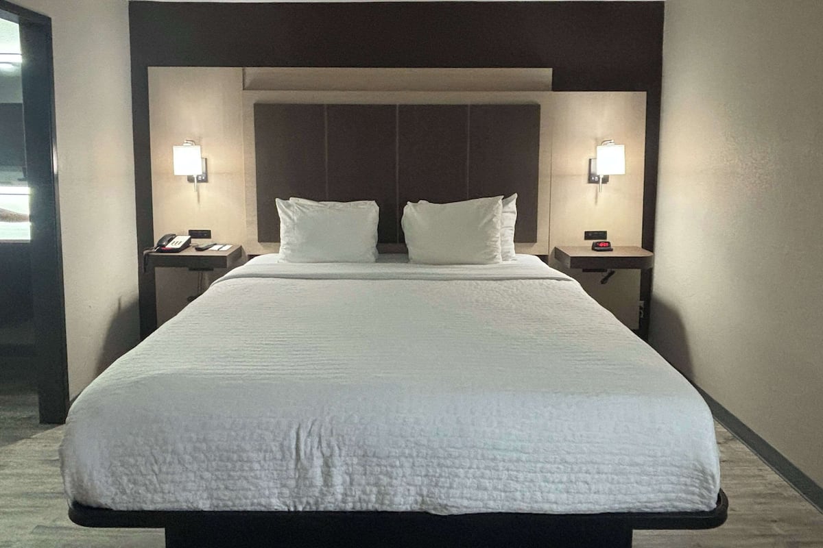 A hotel room with a large bed, two bedside tables, and wall-mounted lamps.