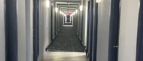 A long, narrow hotel corridor with doors on both sides and a carpeted floor.