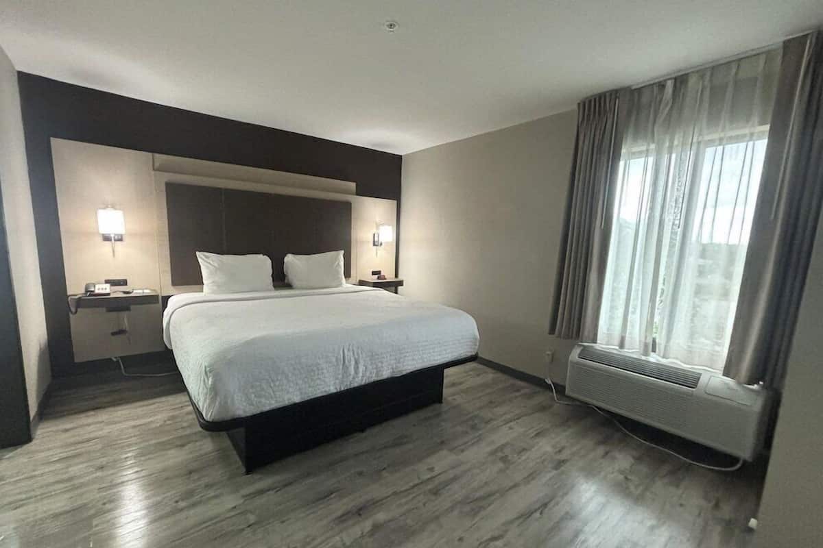 A hotel room with a large bed, bedside tables, a desk, and a window with curtains.