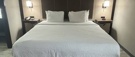 A large bed with a wooden headboard, two bedside tables with lamps, and a telephone on one of the tables.