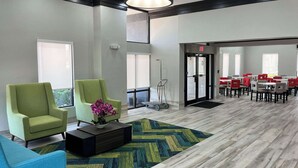 A modern lobby with green armchairs, a coffee table, and a patterned rug.