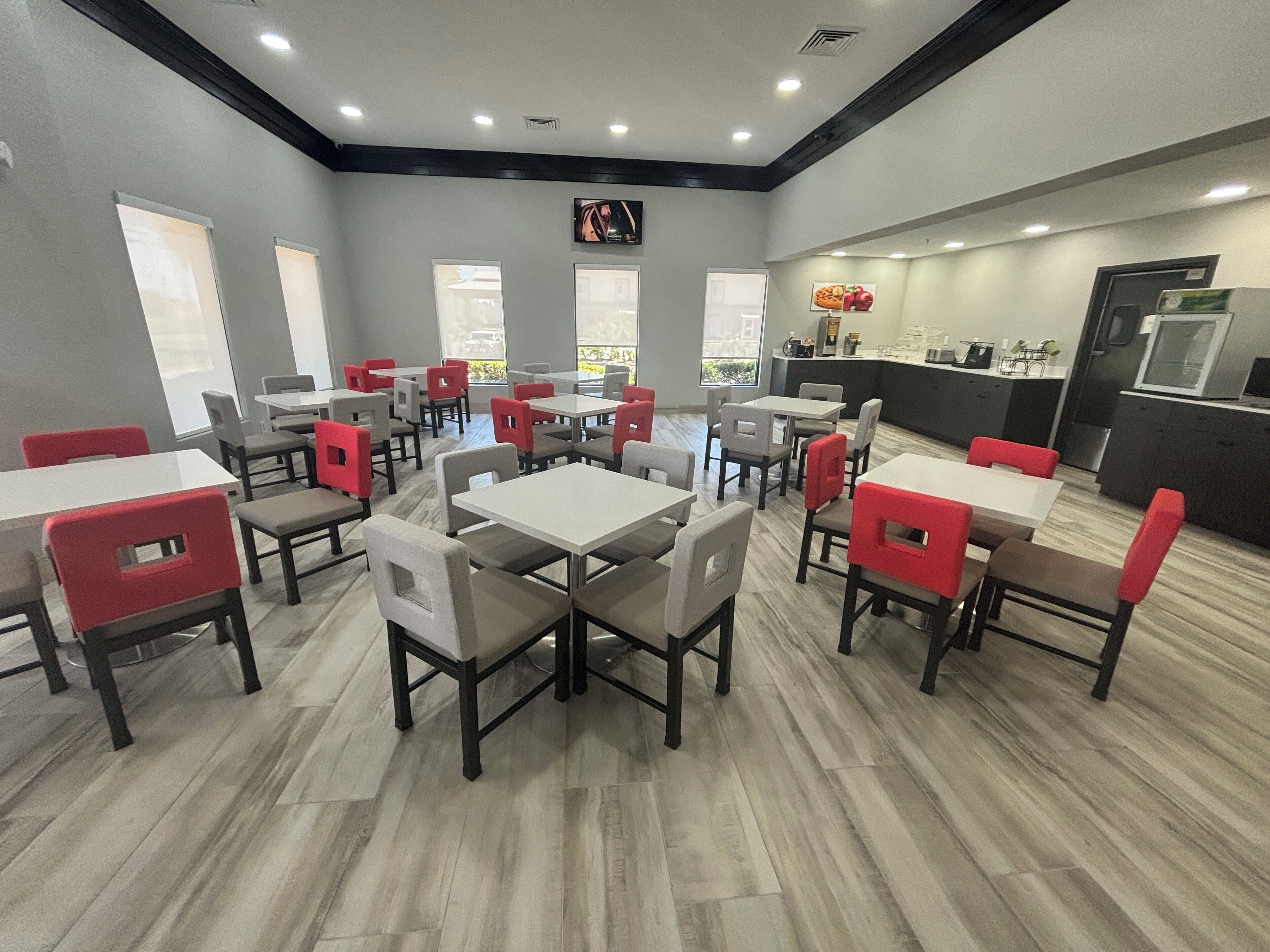 A restaurant with multiple tables and chairs, a kitchen area, and large windows.