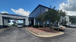 A modern building with a covered entrance, a parking lot, and a tree-lined driveway.