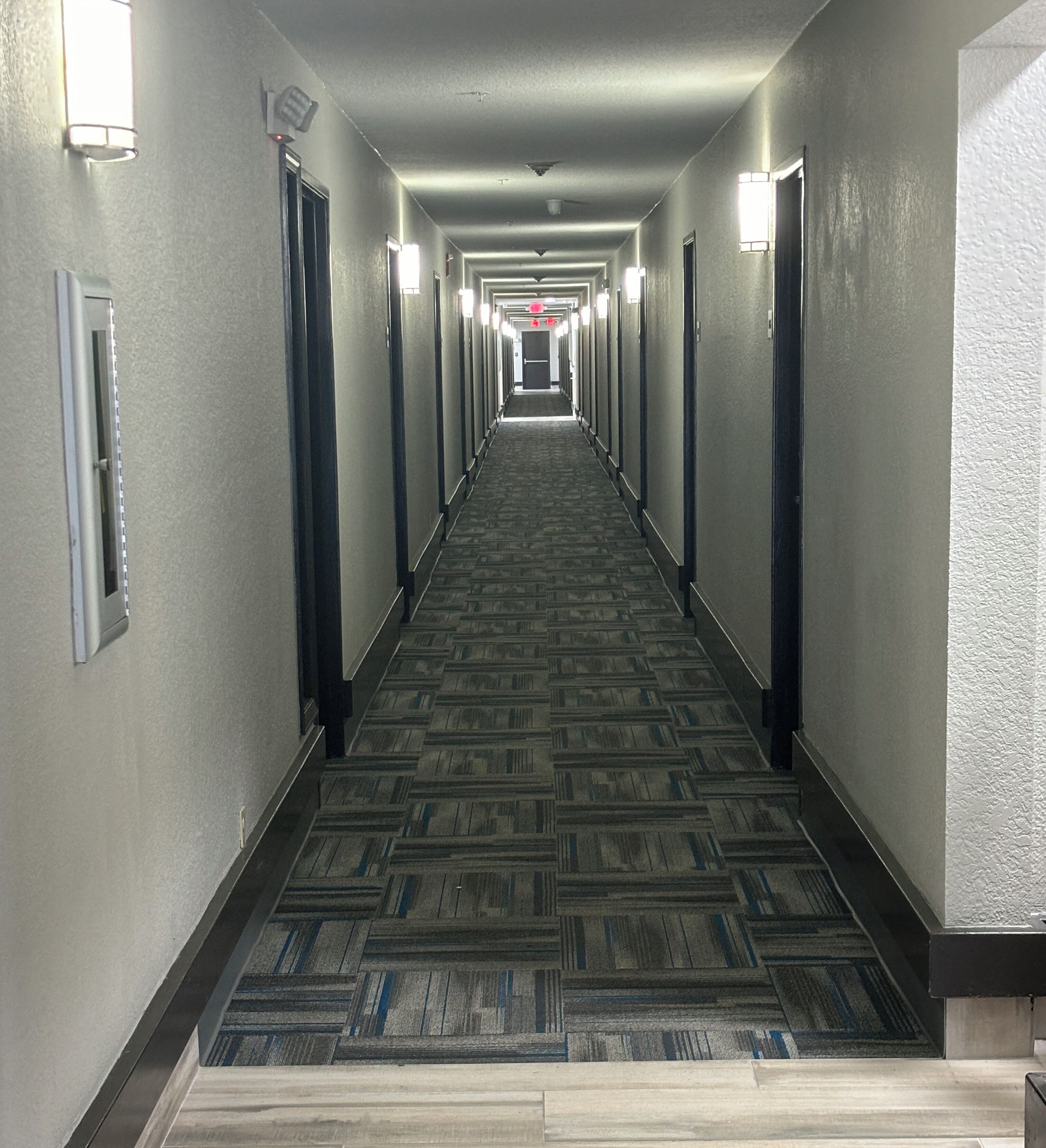 A long, narrow hotel corridor with carpeted flooring and doors on both sides.