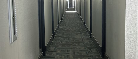 A long, narrow hotel corridor with carpeted flooring and doors on both sides.