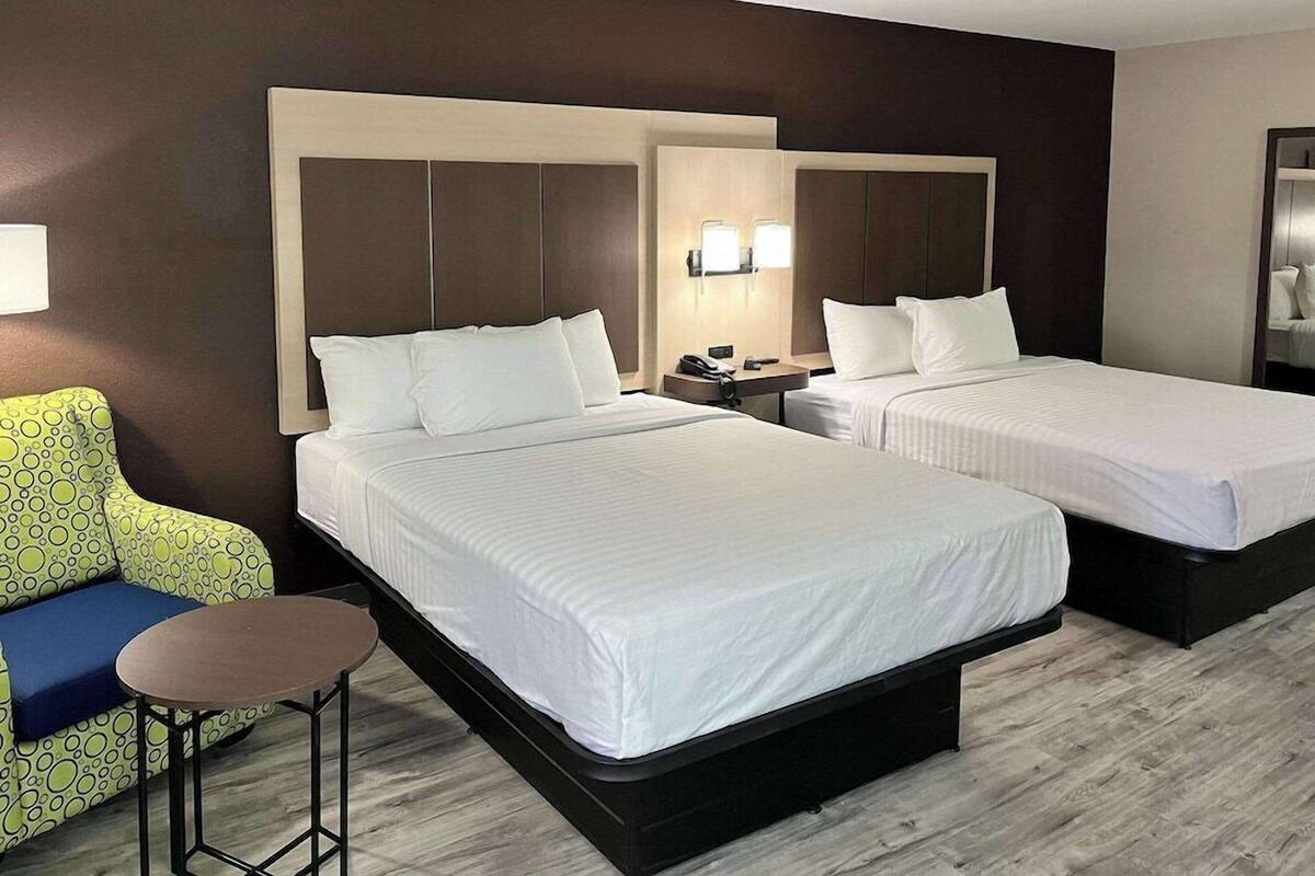A hotel room with two beds, a small table, a sofa, and a mirror.