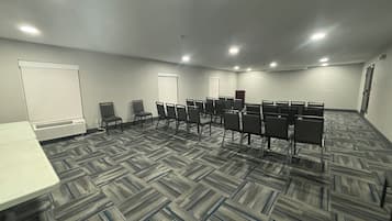Une salle de conférence dotée d’un sol recouvert de moquette, de rangées de chaises, d’un tableau blanc et d’un pupitre.