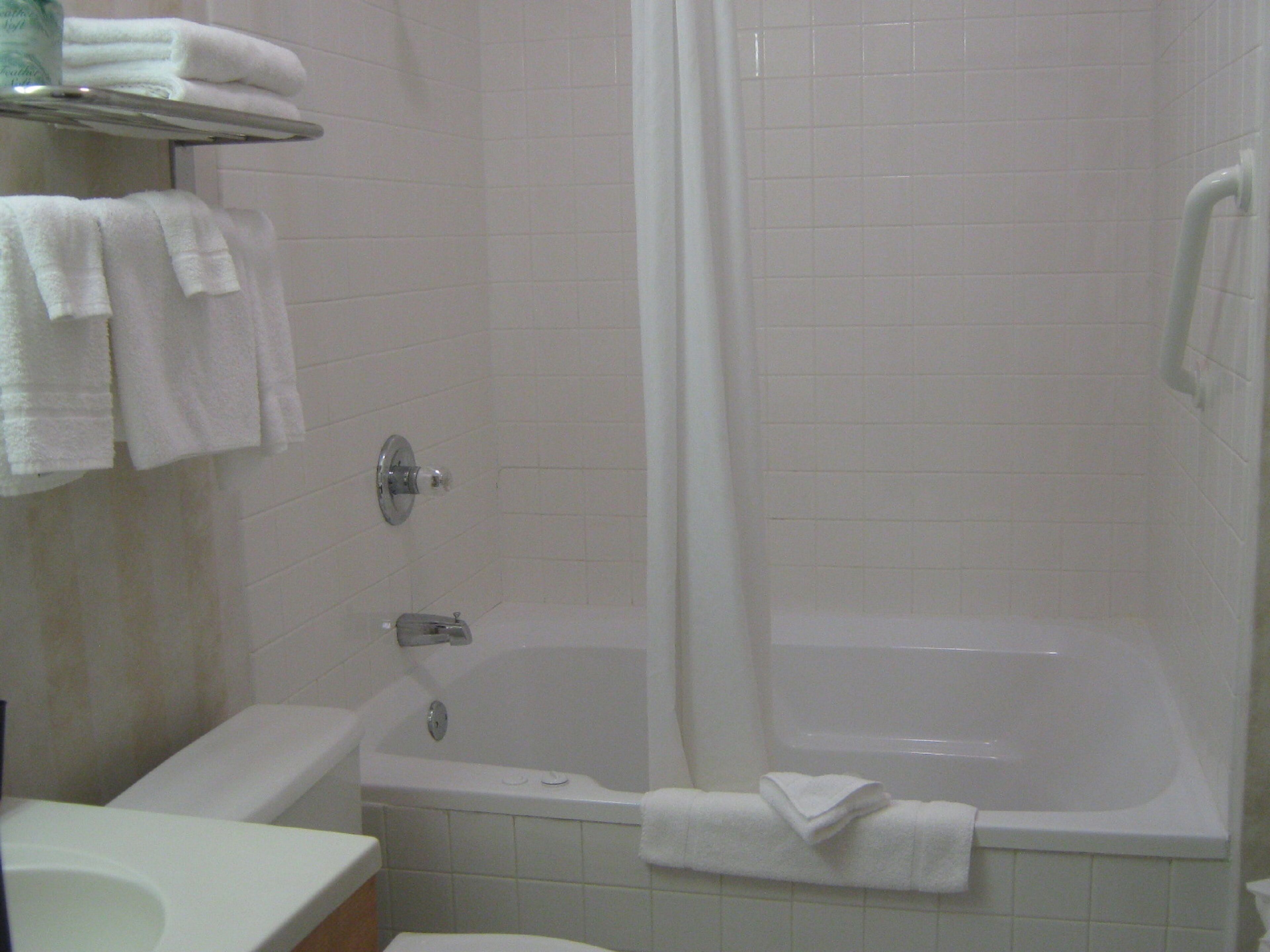 A bathroom with a bathtub, a toilet, and a sink. There are towels on the wall and a shower curtain.